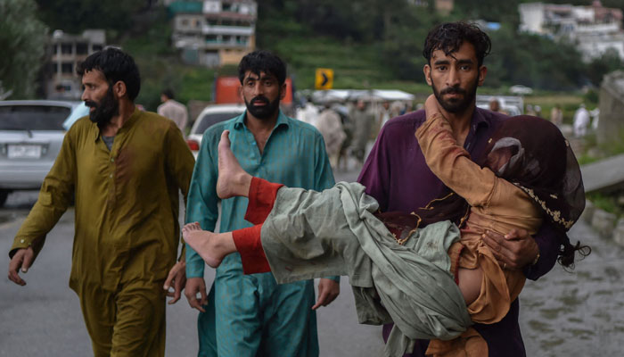 A man (R) carries his sick daughter along a road damaged by flood waters following heavy monsoon rains in Madian area in Pakistan´s northern Swat Valley on August 27, 2022. — AFP