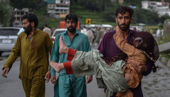 A man (R) carries his sick daughter along a road damaged by flood waters following heavy monsoon rains in Madian area in Pakistan´s northern Swat Valley on August 27, 2022. — AFP