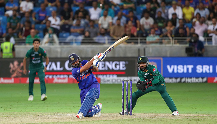 Indian skipper Rohit Sharma swings his bat while Pakistans wicket-keeper Mohammad Rizwan takes position to take a catch. — AFP