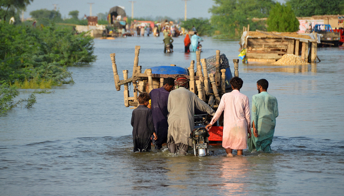 28 اگست 2022 کو پاکستان کے شہر صحبت پور میں بارشوں اور سیلاب کے بعد مرد اپنے سامان کے ساتھ سیلاب زدہ سڑک پر چل رہے ہیں۔ - رائٹرز