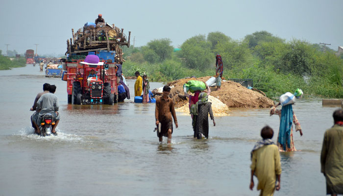 People wade through floodwater along with their belongings at the National High Way in Sohbatpur to reach the safe place on August 29, 2022. ONLINE