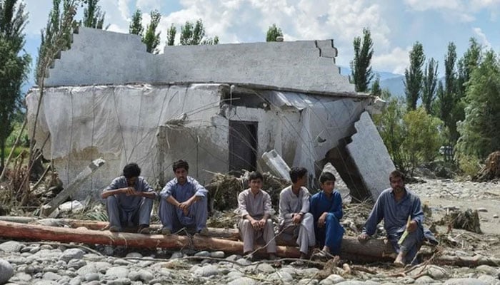Flood-affected people sit beside a wrecked house along a river following heavy monsoon rains in Mingora, a town in Pakistans northern Swat valley on August 28, 2022. — AFP