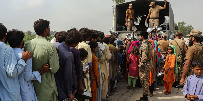 پاکستانی فوج کے اہلکار 27 اگست 2022 کو صوبہ پنجاب کے ضلع راجن پور میں مون سون کی شدید بارشوں کے بعد ایک عارضی کیمپ کے قریب سیلاب سے متاثرہ لوگوں میں کھانا تقسیم کر رہے ہیں۔ — اے ایف پی