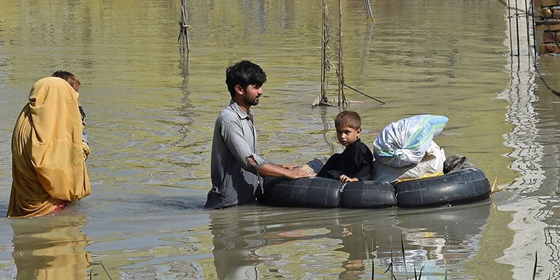 A man pushes a tube carrying his child as he wades through flood water while his wife follows him. — AFP