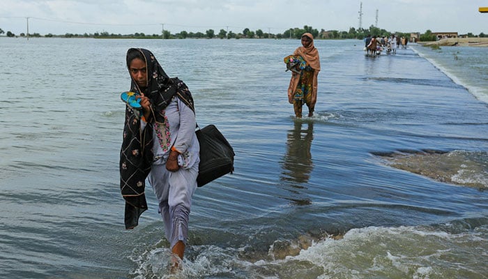 Displaced women wade through a flooded area after heavy monsoon rainfall in Rajanpur district of Punjab province on August 25, 2022. — AFP