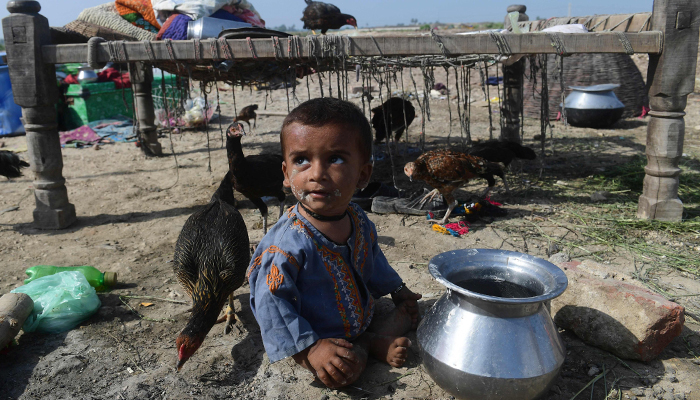 A child sits on a dry ground near by his family after fleeing from flood hit home in Shikarpur of Sindh province on August 30, 2022. — AFP