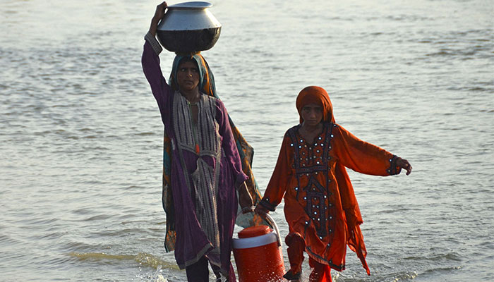Flood affected women carry drinking water in containers after fleeing from their flood hit homes following heavy monsoon rains at Sohbatpur area in Jaffarabad district of Balochistan province on August 28, 2022. — AFP