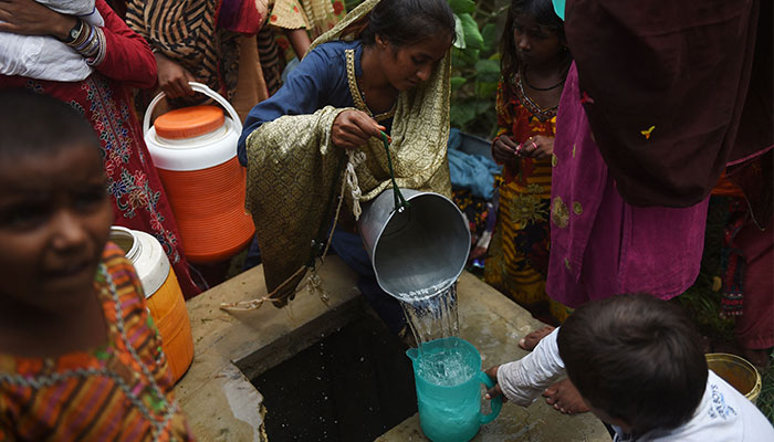 Displaced families who fled from flood hit areas in Sindh province collect water from a well as they take temporary shelter at a government school on the outskirts of Karachi on August 30, 2022. — AFP