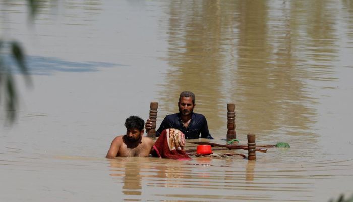 Men wade through flood waters with their belongings in Charsadda, Pakistan August 28, 2022. — Reuters