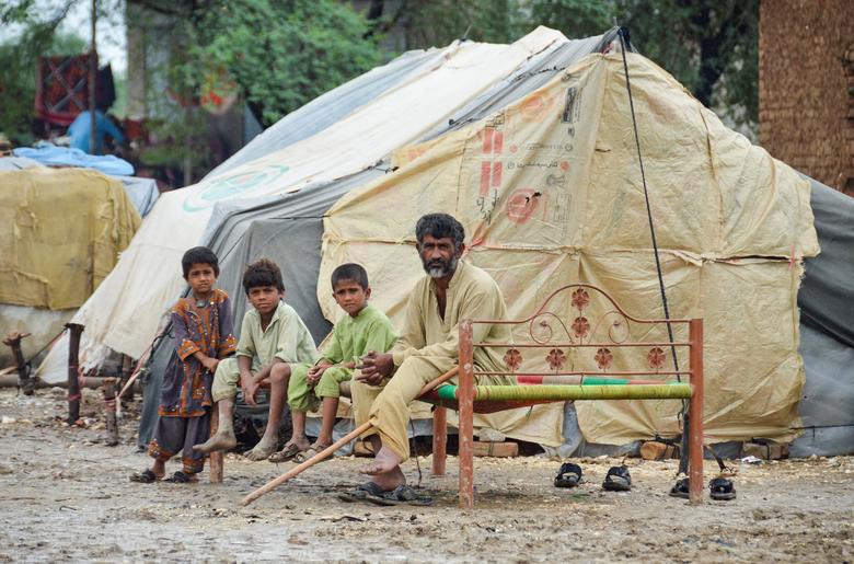 جعفرآباد، پاکستان میں 26 اگست 2022 کو مون سون کے موسم کے دوران بارشوں اور سیلاب کے بعد، ایک آدمی اور بچے اونچی زمین پر دوسروں کے ساتھ پناہ لینے کے بعد اپنے خیمے کے باہر بیٹھے ہیں۔