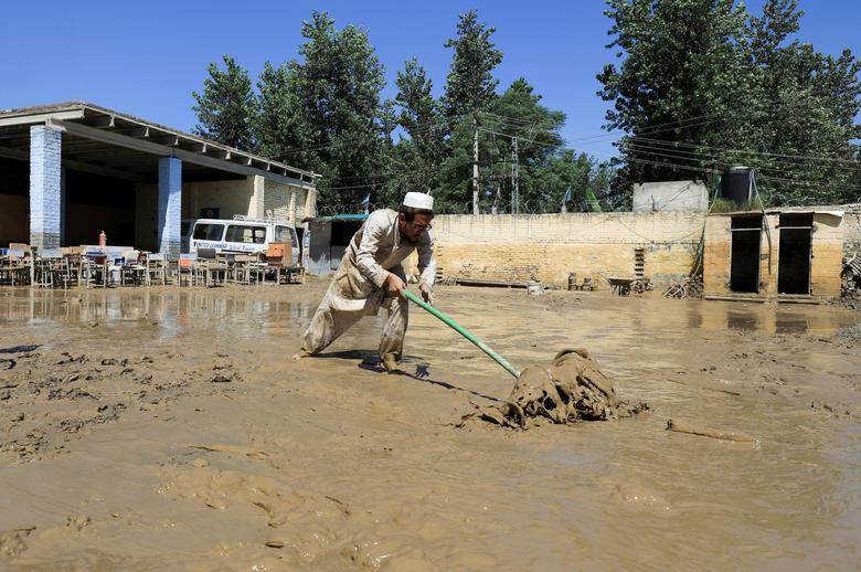 چارسدہ، پاکستان میں 28 اگست 2022 کو مون سون کے موسم کے دوران بارشوں اور سیلاب کے بعد ایک شخص زمین سے کیچڑ صاف کر رہا ہے۔