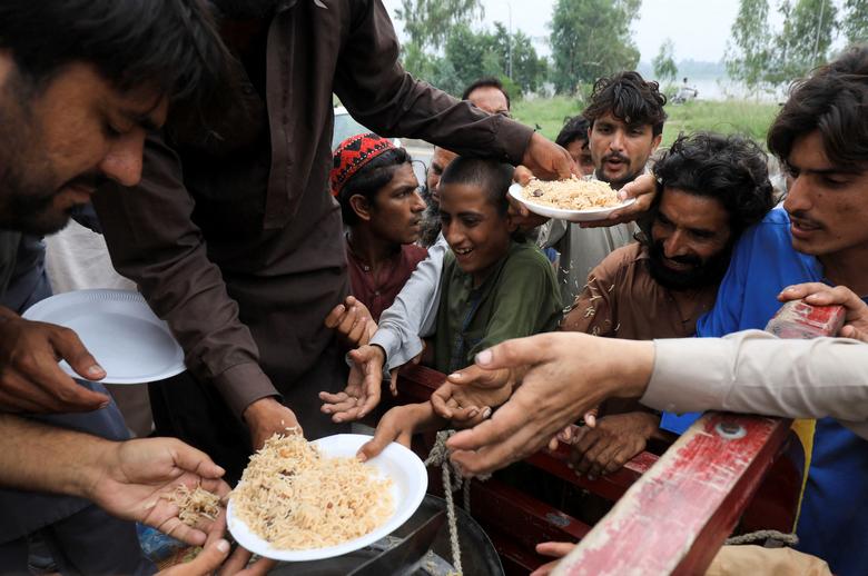 Flood victims receive boiled rice from relief workers, after taking refuge on a motorway, following rains and floods during the monsoon season in Charsadda, Pakistan August 27, 2022.