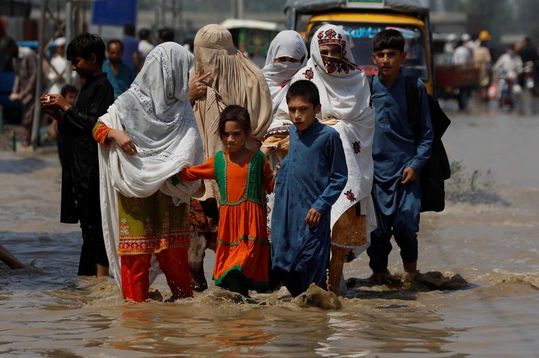 نوشہرہ، پاکستان میں 30 اگست کو مون سون کے موسم کے دوران بارشوں اور سیلاب کے بعد ایک خاندان سیلاب زدہ سڑک پر چل رہا ہے۔