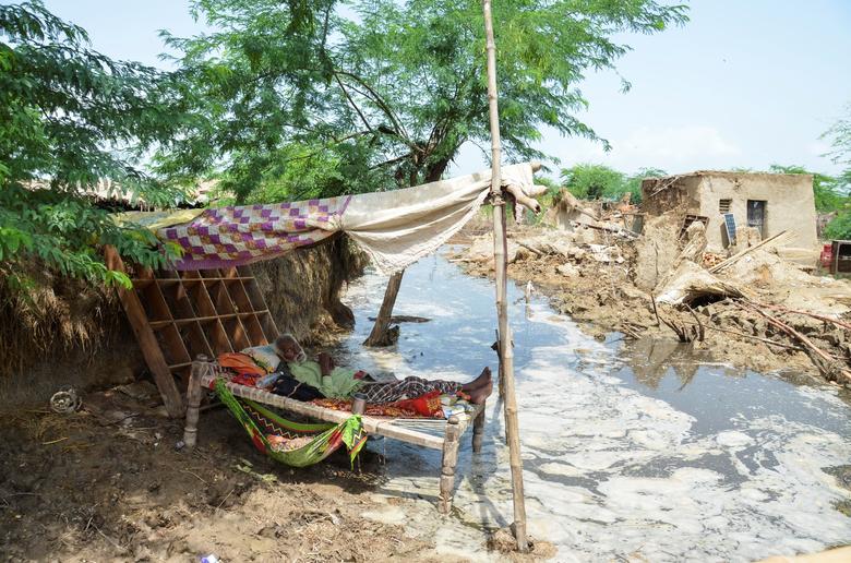 A man rests on a cot made with tope amid flood waters in front of his damaged house following rains and floods during the monsoon season in Jafarabad, Pakistan August 28.