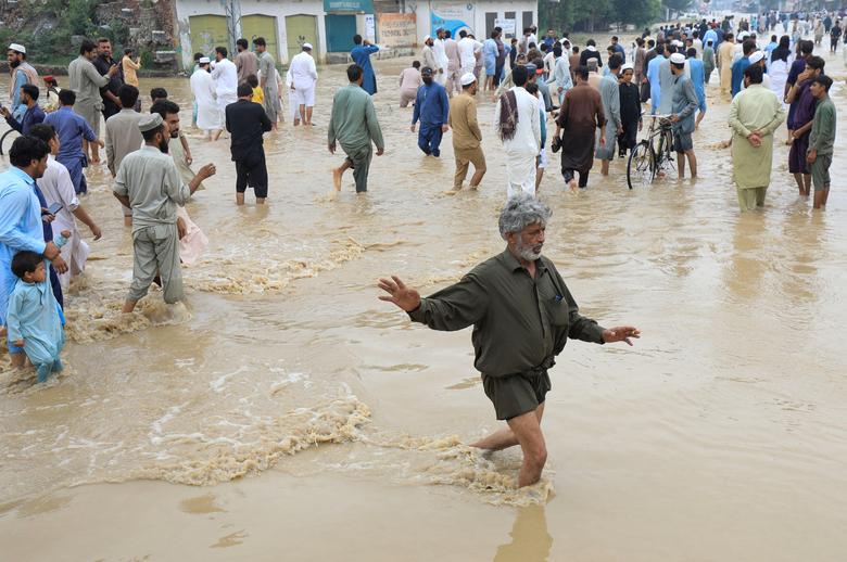 27 اگست، 2022 کو چارسدہ، پاکستان میں مون سون کے موسم کے دوران بارشوں اور سیلاب کے بعد، ایک آدمی اپنے آپ کو متوازن بنا رہا ہے، دوسروں کے ساتھ، سیلاب زدہ سڑک پر چل رہا ہے۔