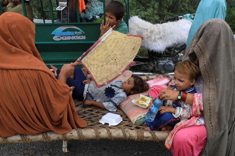 27 اگست 2022 کو چارسدہ، پاکستان میں مون سون کے موسم کے دوران بارشوں اور سیلاب کے بعد، موٹر وے پر پناہ لینے کے بعد خواتین اور بچے اپنے خیمے کے باہر بیٹھے ہیں۔