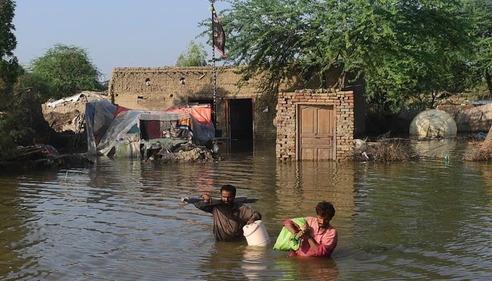 Flood-affected people carry belongings out from their flooded home in Shikarpur, Sindh province, on August 31, 2022. — AFP