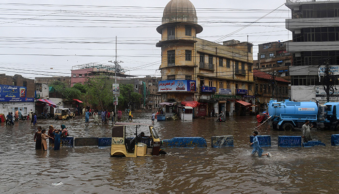 25 جولائی 2022 کو کراچی میں مون سون کی شدید بارشوں کے بعد لوگ سیلاب سے بھری گلی میں گھوم رہے ہیں۔ - AFP