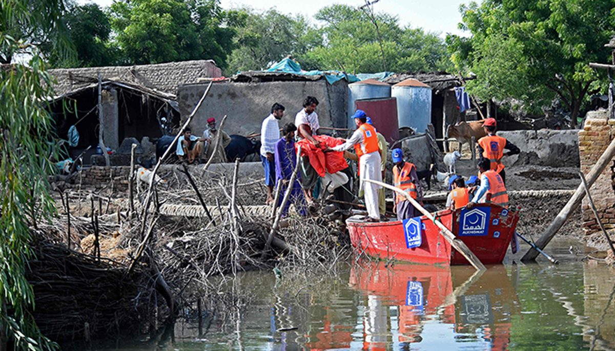 چیریٹی الخدمت فاؤنڈیشن کے رضاکار 31 اگست 2022 کو صوبہ سندھ میں سکھر کے سیلاب زدہ علاقے کے مضافات میں ایک گاؤں میں سیلاب سے متاثرہ لوگوں میں امدادی سامان تقسیم کرنے کے لیے ایک کشتی کا استعمال کر رہے ہیں۔ — اے ایف پی