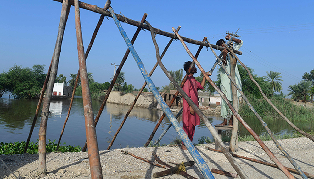 Flood affected people set up a tent in higher ground near the flooded home (background) in Shikarpur, Sindh province, on August 31, 2022. — AFP