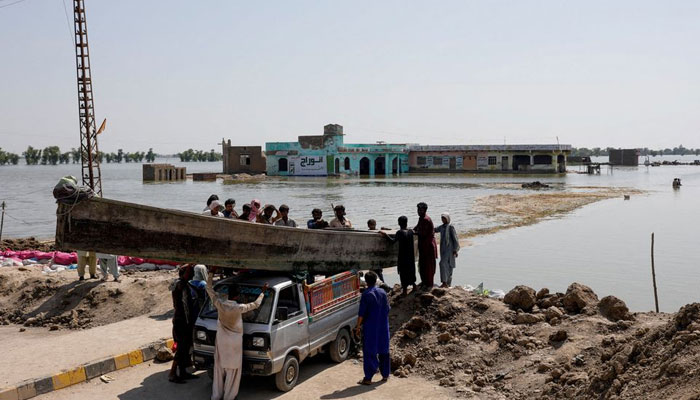31 اگست 2022 کو پاکستان کے میہڑ میں مون سون کے موسم میں بارشوں اور سیلاب کے بعد لوگ انڈس ہائی وے پر بڑھتے ہوئے سیلابی پانی میں لکڑی کی کشتی چلا رہے ہیں۔ — رائٹرز