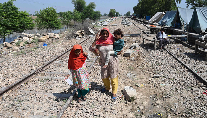 Fahmidah, a pregnant flood-affected woman carries her child as she walks near her tent at a makeshift camp along a railway track in Fazilpur, Rajanpur district of Punjab province on September 3, 2022. — AFP