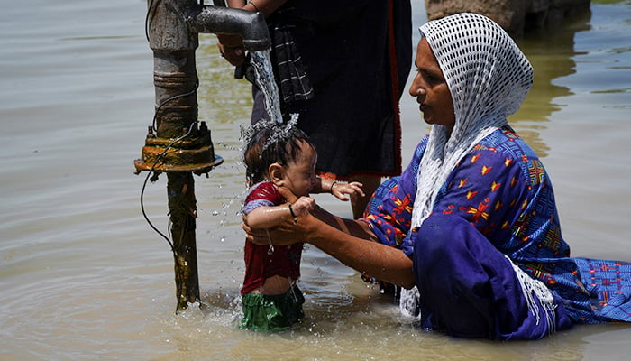 3 ستمبر 2022 کو خیرپور ناتھن شاہ، پاکستان میں مون سون کے موسم کے دوران بارشوں اور سیلاب کے بعد ایک خاتون اپنے سیلاب زدہ گھر کے باہر اپنے بچے کو غسل دے رہی ہے۔ — رائٹرز