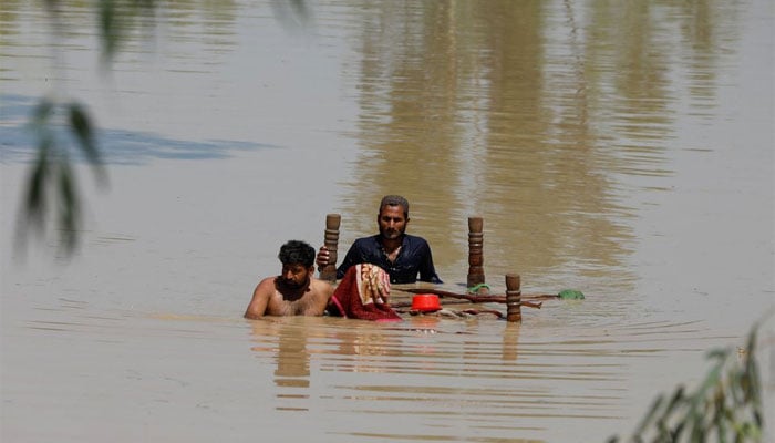 Men wade through flood waters with their belongings in a flood hit area in Pakistan. — Reuters/File