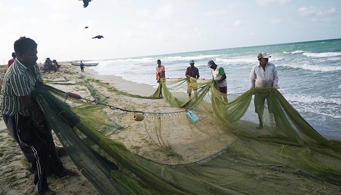 A group of local fishermen attempt to clean an empty fishing net that has just been pulled to shore in Mannar, Sri Lanka, August 17, 2022. — Reuters