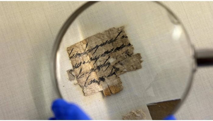 An Israel Antiquities Authority conservator views under a magnifying glass the papyrus fragment at its conservation lab in Jerusalem. — AFP