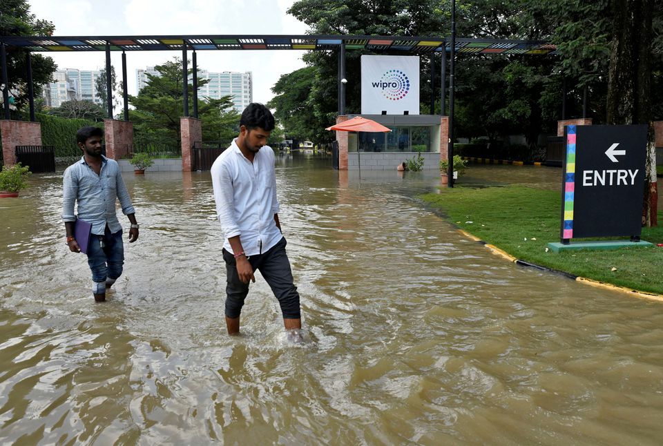 People wade through a waterlogged road in front of the entrance of IT major Wipro Ltd following torrential rains in Bengaluru, India, September 5, 2022.