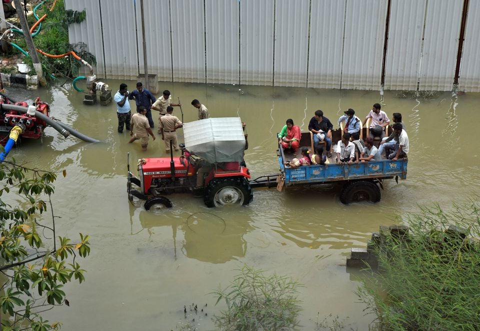 People commute in a tractor trolley as firemen stand next to pumps that are used to remove water from a water-logged neighbourhood following torrential rains in Bengaluru, India, September 7, 2022.