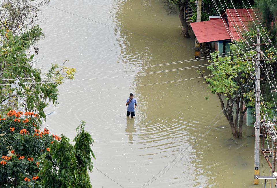 ایک شخص اپنے موبائل فون پر بات کر رہا ہے جب وہ 7 ستمبر 2022 کو بنگلورو، انڈیا میں طوفانی بارشوں کے بعد رہائشی علاقے میں پانی بھری سڑک سے گزر رہا ہے۔