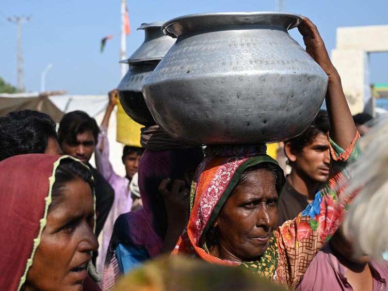 Internally displaced flood-affected women carry water pots at a makeshift camp in Mehar city after heavy monsoon rains in Dadu district, Sindh province on September 9, 2022. — AFP