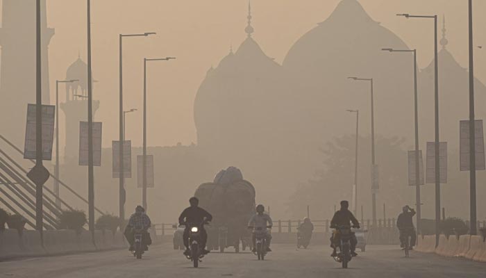Commuters ride along a road amid smoggy conditions in Lahore on November 16, 2021. — AFP/File