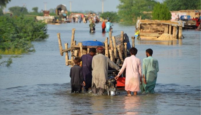 Men walk along a flooded road with their belongings, following rains and floods during the monsoon season in Sohbatpur, Pakistan August 28, 2022. —Reuters