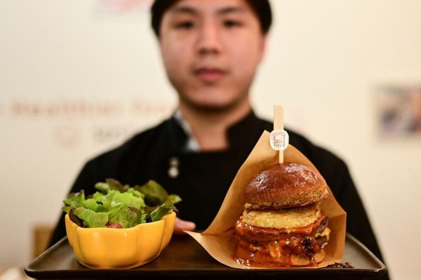 Owner of Bounce Burger, Pooripat Thiapairat, posing with a plate of Cricket-burger, at his restaurant in Bangkok.  — AFP