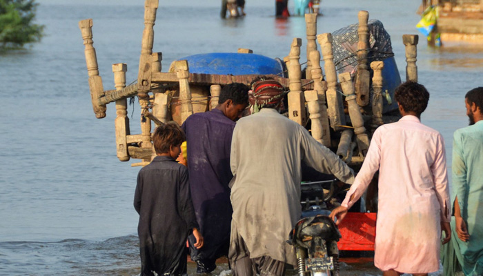 Men walk along a flooded road with their belongings, following rains and floods during the monsoon season in Sohbatpur, Pakistan August 28, 2022. — Reuters