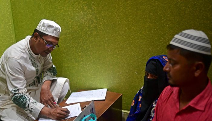 a shrine official prepares a checklist for Ferdousi Begum (C), who consulted Sufi leader Syed Emdadul Hoque (not pictured), at the Maizbhandar Darbar Sharif shrine in Maizbhandar. Evil spirits bedevil the families that seek blessings from an elderly Bangladeshi mystic— but he knows that his prayers alone are not enough to soothe their troubled minds. — AFP