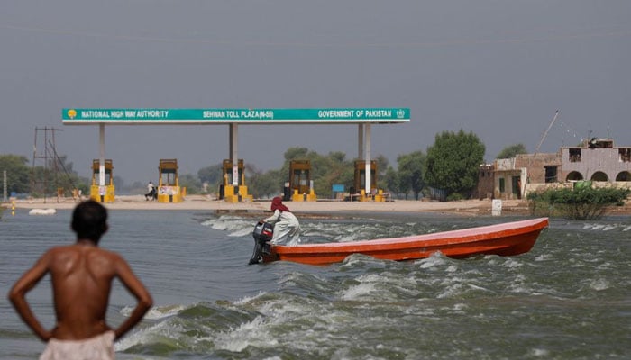 Seorang pria mengendarai perahu melewati alun-alun tol di tengah banjir di jalan raya utama Indus, menyusul hujan dan banjir selama musim hujan di Sehwan, Pakistan, 15 September 2022. — Reuters