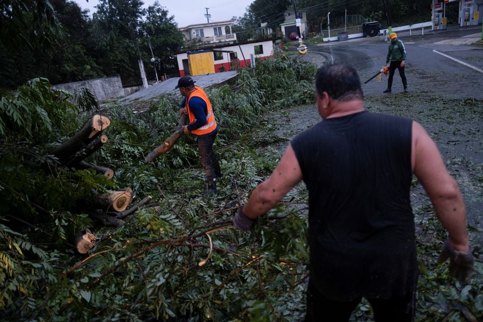 18 ستمبر 2022 کو پورٹو ریکو کے یوکو میں سمندری طوفان فیونا کے علاقے کو متاثر کرنے کے بعد لوگ گرے ہوئے درخت سے سڑک صاف کر رہے ہیں۔