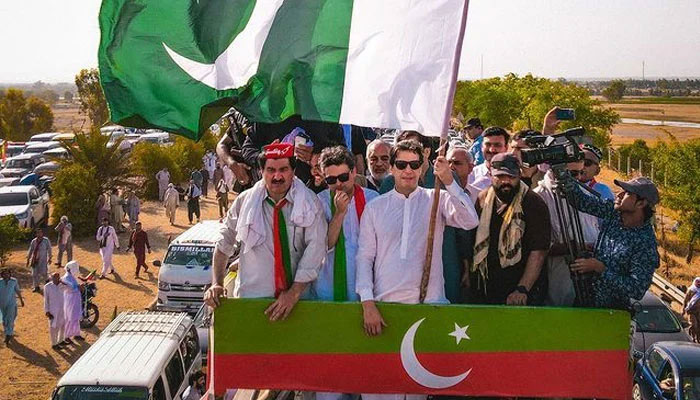 PTI Chairman Imran Khan (centre) holds a flag of Pakistan on top of a rally container in this undated photo. — Twitter/PTI