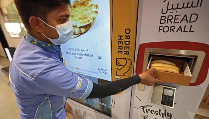 A man collects items from a vending machine that gives out free bread in Dubai. — AFP