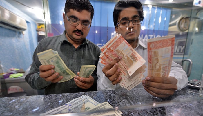 Money dealers counts Pakistani rupees (R) and US dollars at a currency exchange in Islamabad, Pakistan, on March 12, 2014