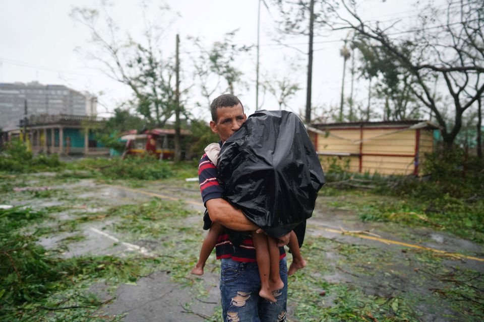 27 ستمبر، 2022 کو پنار ڈیل ریو، کیوبا میں گزرنے کے بعد ایک شخص اپنے بچوں کو سمندری طوفان ایان کے ملبے کے پاس لے جا رہا ہے۔ - رائٹرز
