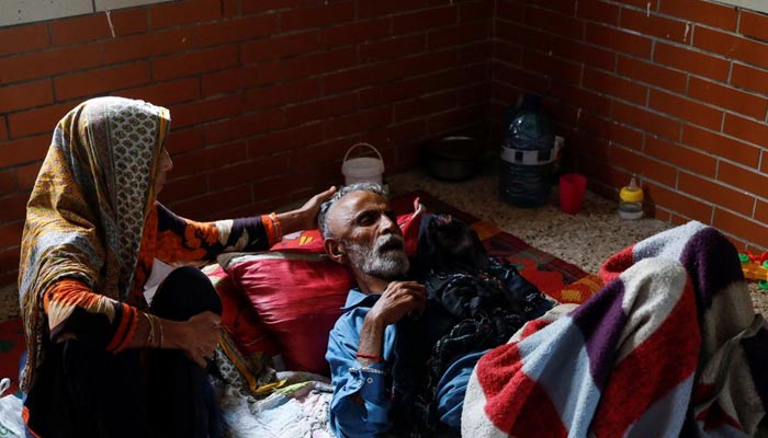 کراچی، پاکستان میں 22 ستمبر، 2022 کو ایک بے گھر خاتون رحمت خاتون اپنے بیمار شوہر 65 سالہ مہدی حسن کی دیکھ بھال کر رہی ہے، جب وہ مون سون کے موسم میں بارشوں اور سیلاب کے بعد ایک اسکول میں پناہ لے رہے ہیں۔ — رائٹرز/فائل