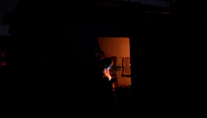 A woman checks her mobile phone while standing by the door at her home during the seven hours power outage in Colombo, Sri Lanka, March 2, 2022. — Reuters/File