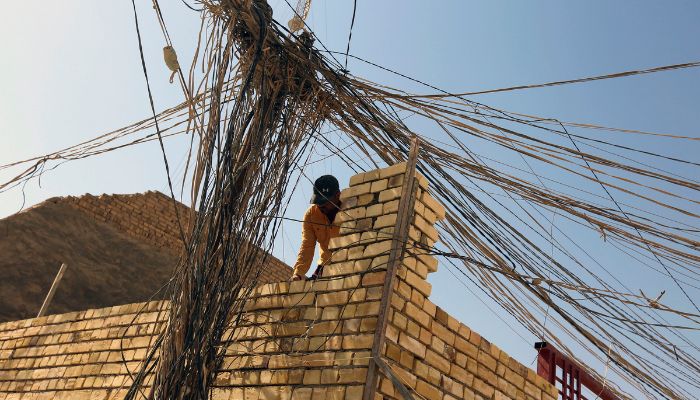 An Iraqi worker stands next to a web of electric wires, used to draw electricity from private generators due to an unreliable national electricity supply, in the Iraqi central city of Karbala on October 3, 2022. —  AFP