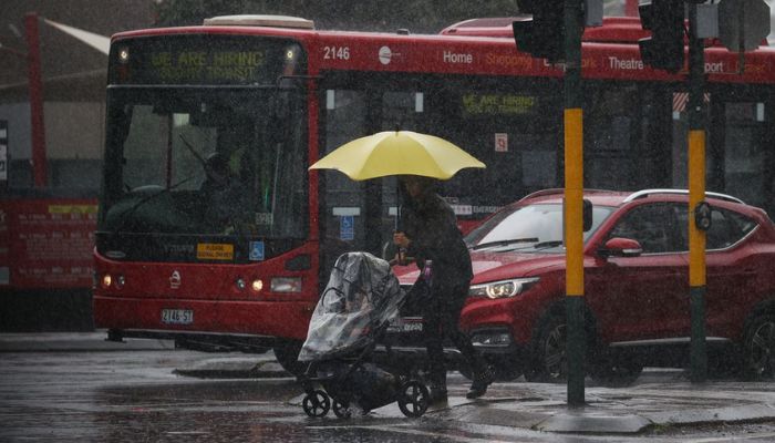 A pedestrian pushing a baby pram crosses a flooding intersection as heavy rains affect Sydney, Australia, October 6, 2022. —  Reuters