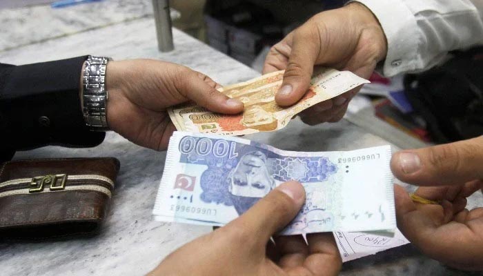 Men exchange Pakistani banknotes at a shop counter in Peshawar, Pakistan, on November 17, 2017. — Reuters
